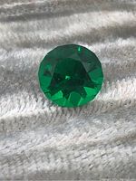 Close-up photo of the round, faceted green emerald gemstone highlighting its color and cut.