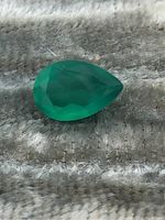 Close-up image of pear-shaped emerald gemstone showing its faceted surface and green color on textured gray fabric.