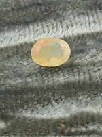 Front view of the oval faceted Ethiopian opal loose gemstone on a textured gray fabric background, showing play-of-color.