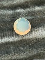 Front photo showing the smooth, faceted round opal with pale orange and blue tones.