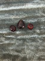 Front view of three garnet gemstones on fabric showing pear-shaped and round cuts.