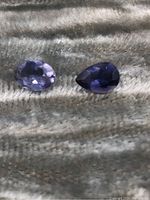 Photo showing two loose iolite gemstones on a fabric surface, one pear-shaped and one oval-shaped, highlighting color and cut.