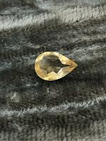 Top view of pear cut Madagascar citrine gemstone on textured fabric background, showing clear facets and golden-yellow color.