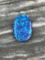 Front view of oval opal cabochon showing vibrant blue and green iridescence on a polished surface.