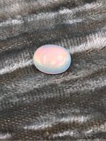 Photo of oval cabochon opal gemstone on textured cloth, showing play of colors and smooth polished surface.