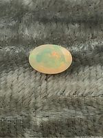 Close-up image of an oval opal gemstone showing its opalescent color play on a textured gray background.