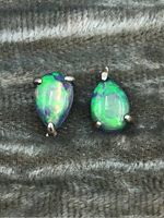 Two pairs of pear-shaped opal gemstones with silver prong settings on textured fabric background showing color play and condition.
