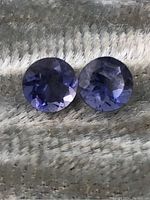 Close-up image of two round faceted iolite gemstones showing their color and cut on a textured surface.