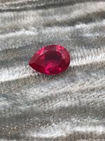 Close-up image of the pear-shaped deep red ruby gemstone showing surface and facets under natural light.