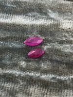 Two marquise-cut ruby gemstones placed on a textured fabric background showing size and color.