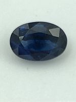 Close-up image showing oval cut sapphire with dark blue color and faceted surface.