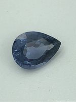 Close-up image showing the pear-shaped spinel gemstone with faceted cut and blue-violet color.