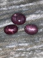 Three star rubies arranged on a textured surface showing color and surface reflection.