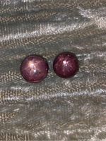 Pair of round star rubies resting on textured fabric, showing front star asterism effect under lighting.