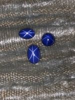 Three star sapphires displayed on textured fabric showing distinct star patterns on polished cabochon surfaces.