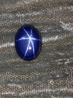 Photo showing top view of the synthetic star sapphire highlighting the six-ray star asterism and deep blue color, placed on textured fabric.