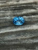 Oval blue topaz gemstone on textured fabric background, showing brilliance and color.
