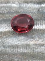 Close-up photo of the oval faceted tourmaline gemstone showing deep reddish-pink color and inclusions under magnification.