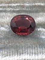 Close-up front view of a 2.55 carat oval faceted tourmaline gemstone showing its rich reddish-pink color and internal facets.