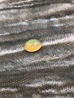 Yellow fire opal gemstone showing translucency and color play on a textured fabric background.
