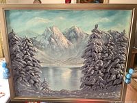 Photo showing original acrylic winter landscape painting with snowy pine trees and mountain lake signed R. Korri in silver frame