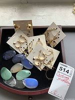 Several pairs of gold-tone earrings on white display cards alongside colorful stone teardrop necklace pieces arranged in a tray.