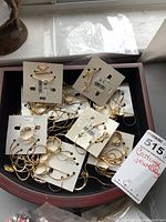 Loose assortment of gold-tone costume necklaces, earrings, and jewelry attached to white display cards in a container, some cards have price tags.