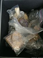 Box with multiple plastic bags containing assorted beads and costume jewelry pieces, mostly glass beads with varied colors and textures.