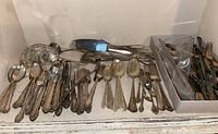 Wide shot of assorted vintage silver-plated cutlery including forks, tablespoons, teaspoons, a fish-shaped serving dish, and napkin stand arranged on a shelf.