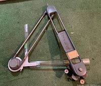 Photo showing the full drafting T-square tool with adjustable arms and clamp, laid flat on green carpet.