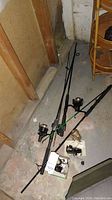Photo of two fishing rods with attached reels and loose reels placed on concrete floor in basement area.