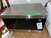 Front and side view of stainless steel LG microwave Model LMC0975SR with digital display on, located on wooden surface.