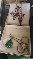 Two necklaces displayed in separate jewelry boxes, one with a triangular green pendant, the other a purple bead beaded necklace.