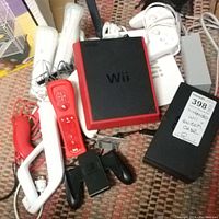 Overview of red and black Nintendo Wii Mini console with multiple Wii Remotes (red and white), Nunchuk controllers, sensor bar, charger, and a black Nintendo Switch case labelled.