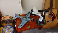 Photo shows Kazam mini toy airplane model B-143 in blue with US Air Force insignia, placed on a small wooden table alongside other toys and items.