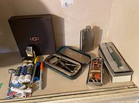 Photo showing UGG sheepskin care kit, lip creams, markers, stainless steel hip flask, Sheaffer fountain pen, and Rolls Razor vintage shaving handle set