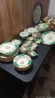 Overview of the vintage Myotts china set arranged on a table showing plates, bowls, teacups, and serving dishes with bird motif and green/gold detailing.