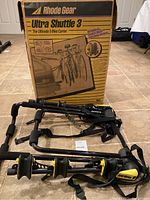 Folded Rhode Gear Ultra Shuttle 3 bike carrier with straps and padded supports visible, positioned on floor with original box in background.