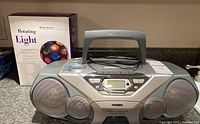 Front view of silver Philips AZ1565 boombox with handle and speakers, next to boxed Radio Shack multicolored rotating light.