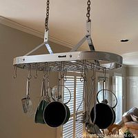 Photo showing the oval-shaped chrome hanging pot rack with multiple hanging pots and kitchen utensils, suspended by metal chains from the ceiling.