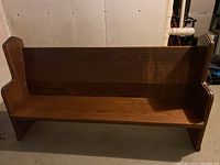 Overall view of the dark brown wooden church pew showing the bench seat and backrest.