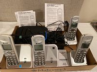 Four AT&T cordless telephone handsets with charging bases connected by multiple cords, plus instruction manuals in background