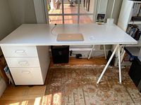 Full view of white melamine desk with three-drawer base unit on casters, showing overall desk and surrounding space.