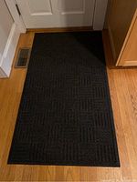 Black entryway mat with geometric textured pattern on wood floor