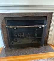 Front view of black wraparound fireguard with pewter-colored trim and handles in place on hearth.