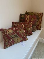 Four cushions with geometric and floral patterns in earthy colors displayed in a row on a white surface.