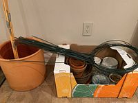 View showing large terracotta pot next to box containing smaller pots, stakes, and stones.
