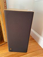 Front view of one JBL speaker showing black fabric grille and small JBL logo at bottom corner.