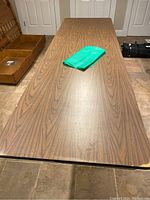 Top view of large folding table with woodgrain laminate surface, folded green cloth placed on top, edges show wear.