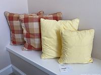 Four cushions displayed in total, two yellow and two checked patterns.